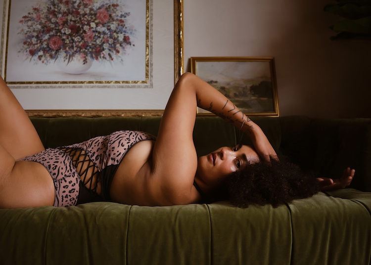 photo of a woman laying on a green couch in a leopard bodysuit looking at the camera