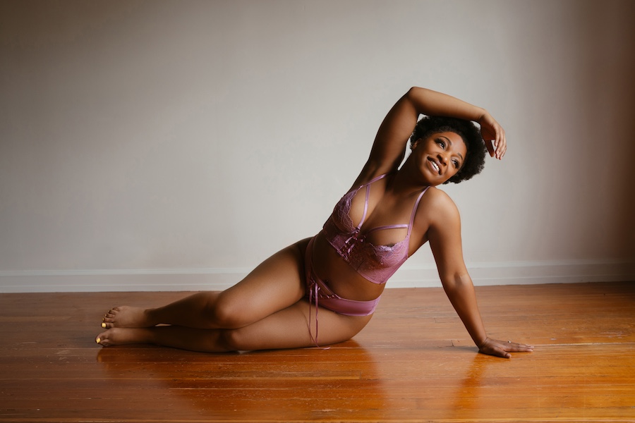 photo of a black woman in purple lingerie sitting on her side and smiling