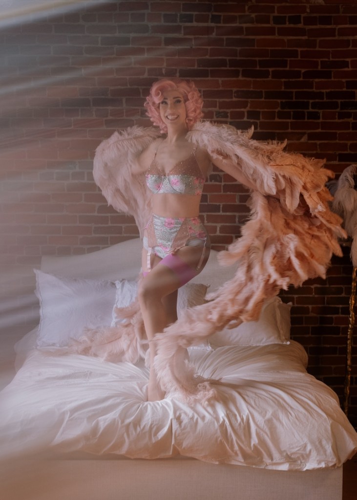 woman wearing pink angel wings posing on a bed