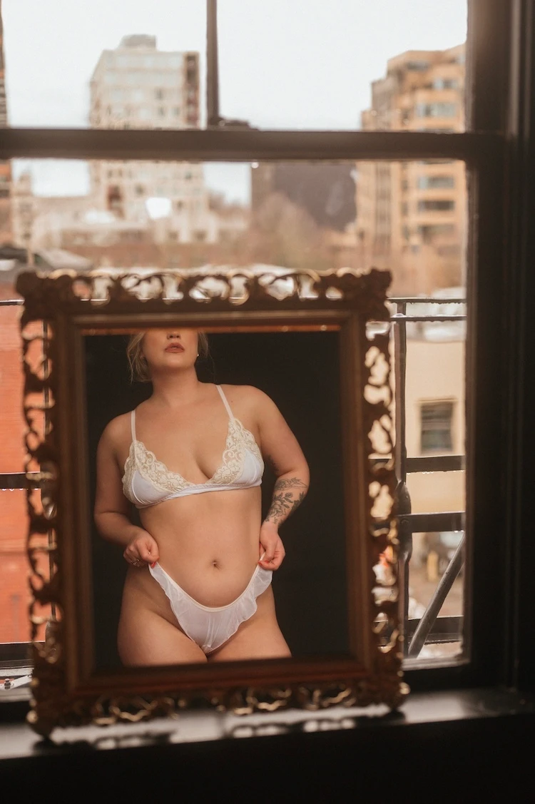 woman draped in green fabric poses on white bed sheets, boudoir photography portland